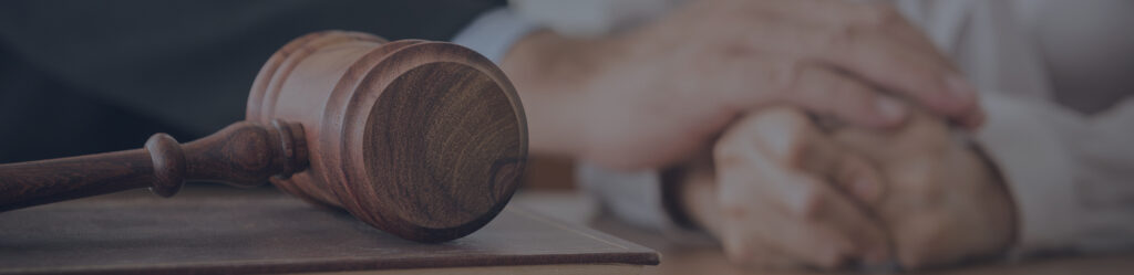 Wooden gavel resting on a desk as two people shake hands in the background, signaling a legal agreement or judgment.