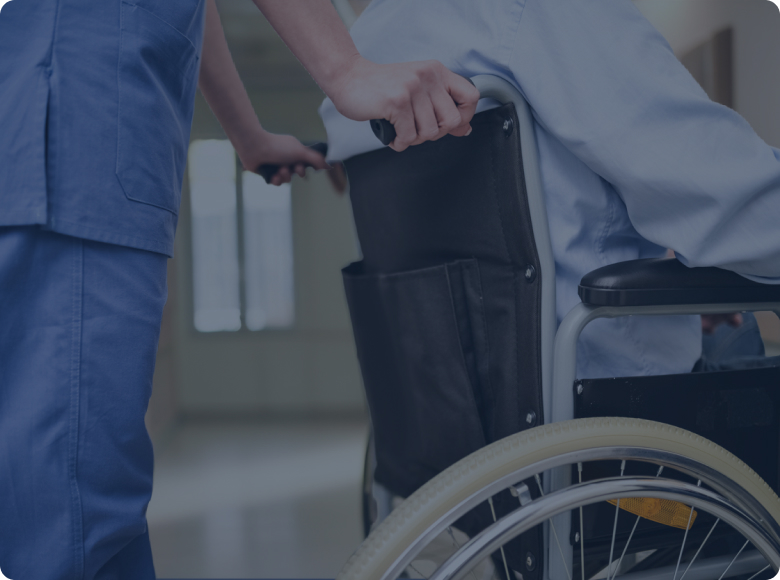Caregiver in blue scrubs pushing a wheelchair with a patient in a hospital corridor